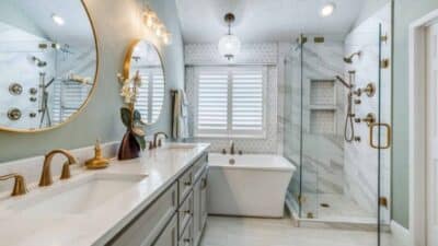 Luxurious modern bathroom with double vanity, marble shower, freestanding tub, round mirrors, and gold fixtures.