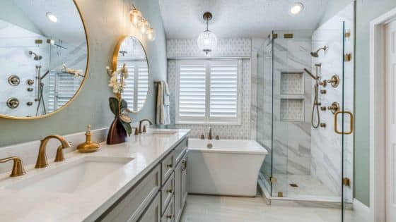 Luxurious modern bathroom with double vanity, marble shower, freestanding tub, round mirrors, and gold fixtures.