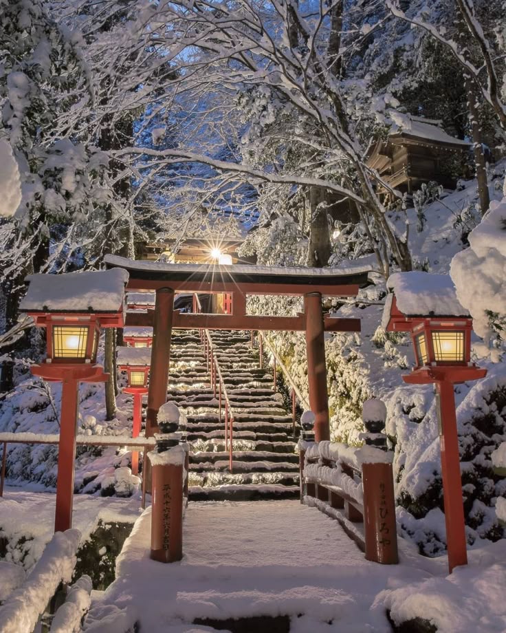 Snow-covered Japanese shrine entrance with red torii gate and lanterns leading up snowy steps in winter.