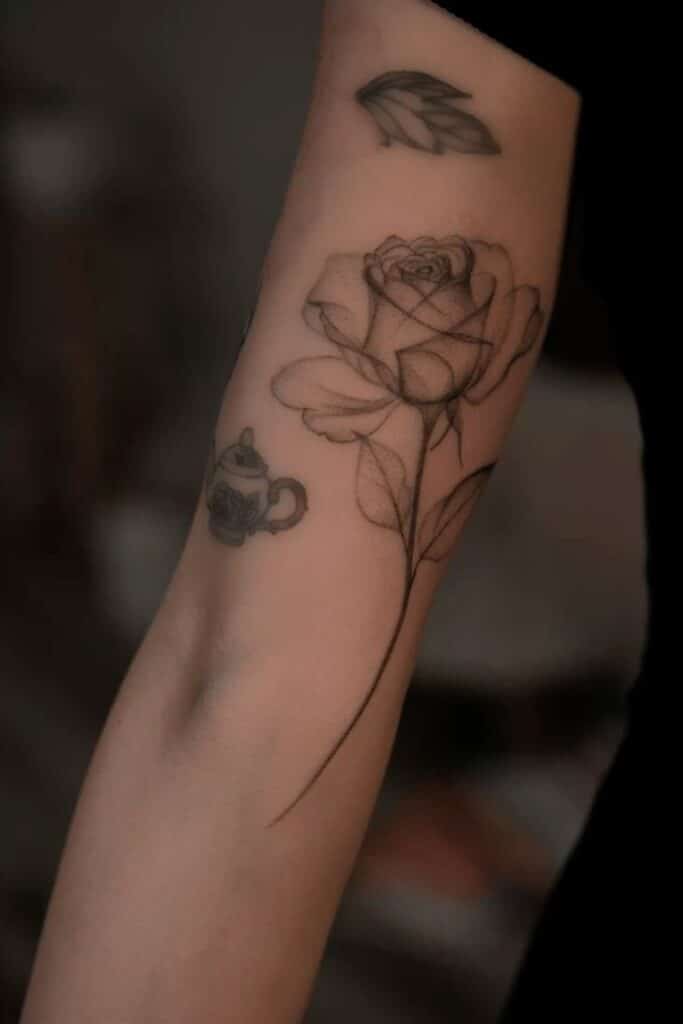 Rose and teapot tattoos on forearm, showcasing intricate black linework and shading. Perfect for body art inspiration.