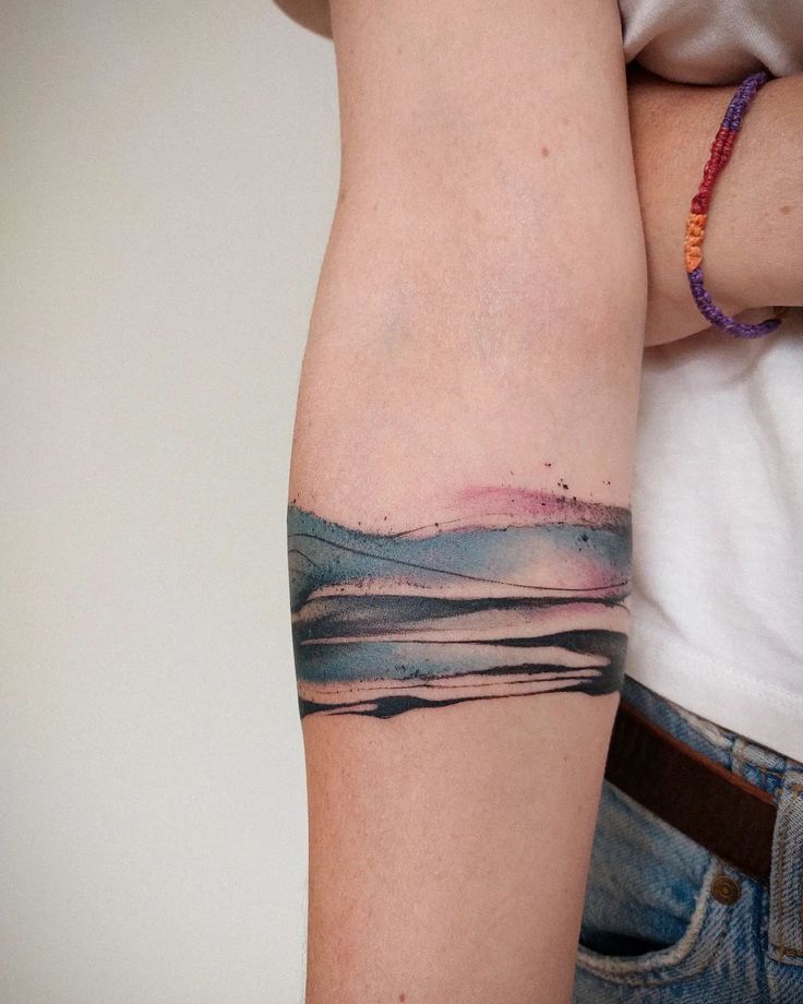 a072d0a9880610e72e84fca79ec63f05 Arm with abstract watercolor tattoo design featuring pink, blue, and black waves, wearing a colorful bracelet. | Sky Rye Design Arm with abstract watercolor tattoo design featuring pink, blue, and black waves, wearing a colorful bracelet.