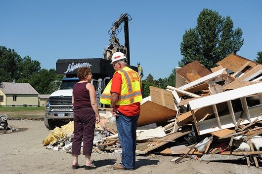 Workers assess debris at a construction site, planning cleanup and waste removal with heavy machinery in the background.