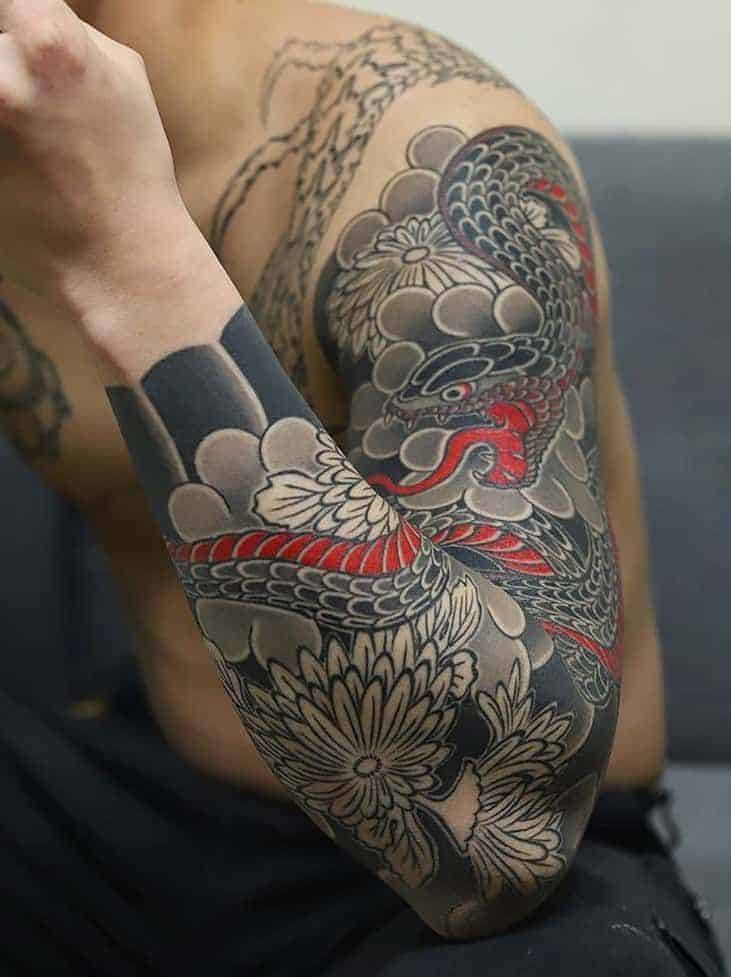 Detailed dragon tattoo sleeve with red and black scales, paired with floral designs, on a person's arm and shoulder.