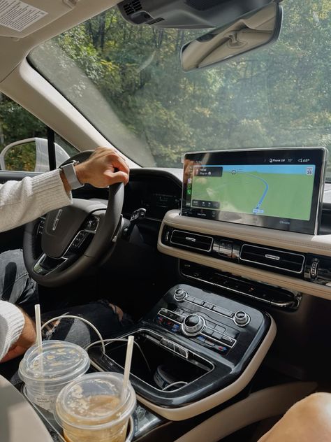 Driving through scenic route with GPS navigation in a modern car interior, featuring drinks and controls on a sunny day.