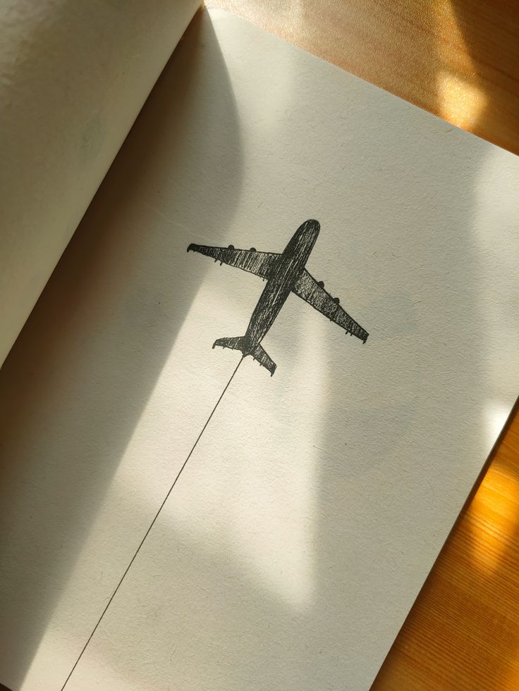 Sketch of an airplane drawn in a notebook, casting a shadow on the page. Sunlight illuminates the surface, creating a warm ambiance.