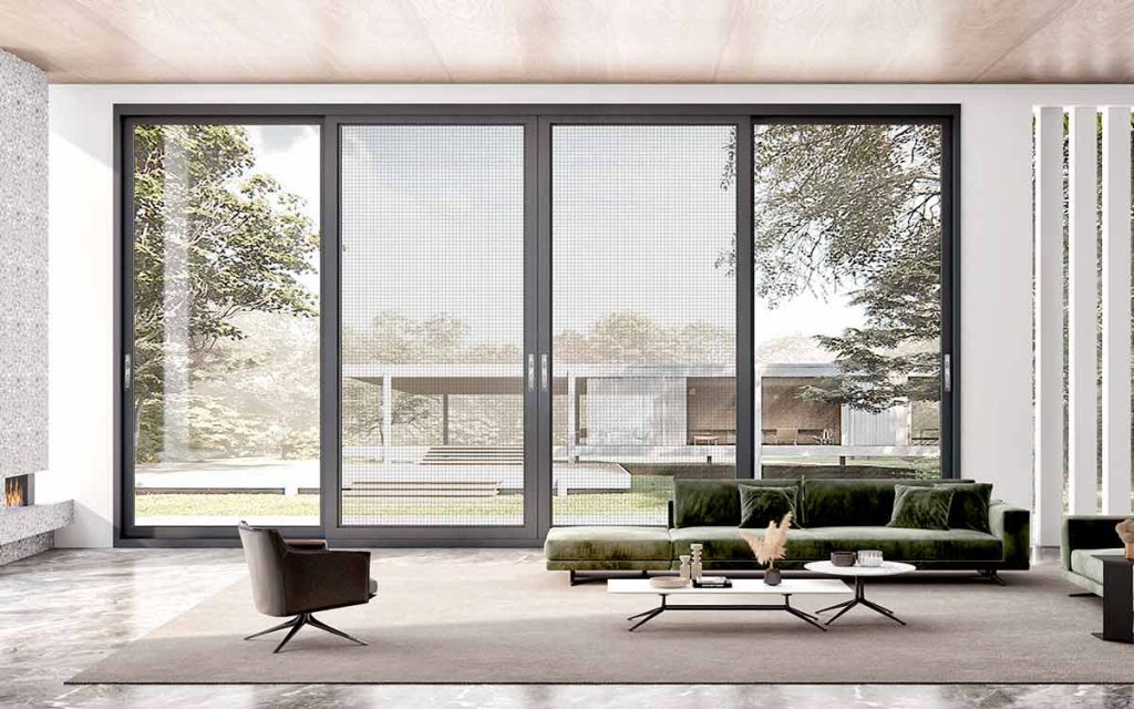 Modern living room with large glass doors, green velvet sofas, and a scenic view, blending indoor and outdoor spaces for a serene atmosphere.