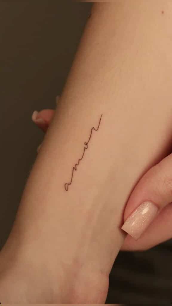 amor Minimalist amor tattoo in cursive script on a person's arm, with delicate detail and a soft focus background. | Sky Rye Design Minimalist amor tattoo in cursive script on a person's arm, with delicate detail and a soft focus background.