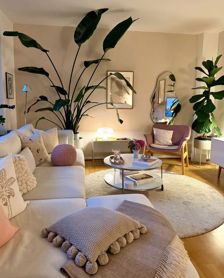 Cozy living room with modern furniture, lush plants, a white sectional sofa, and stylish decor. Warm lighting creates a relaxing ambiance.