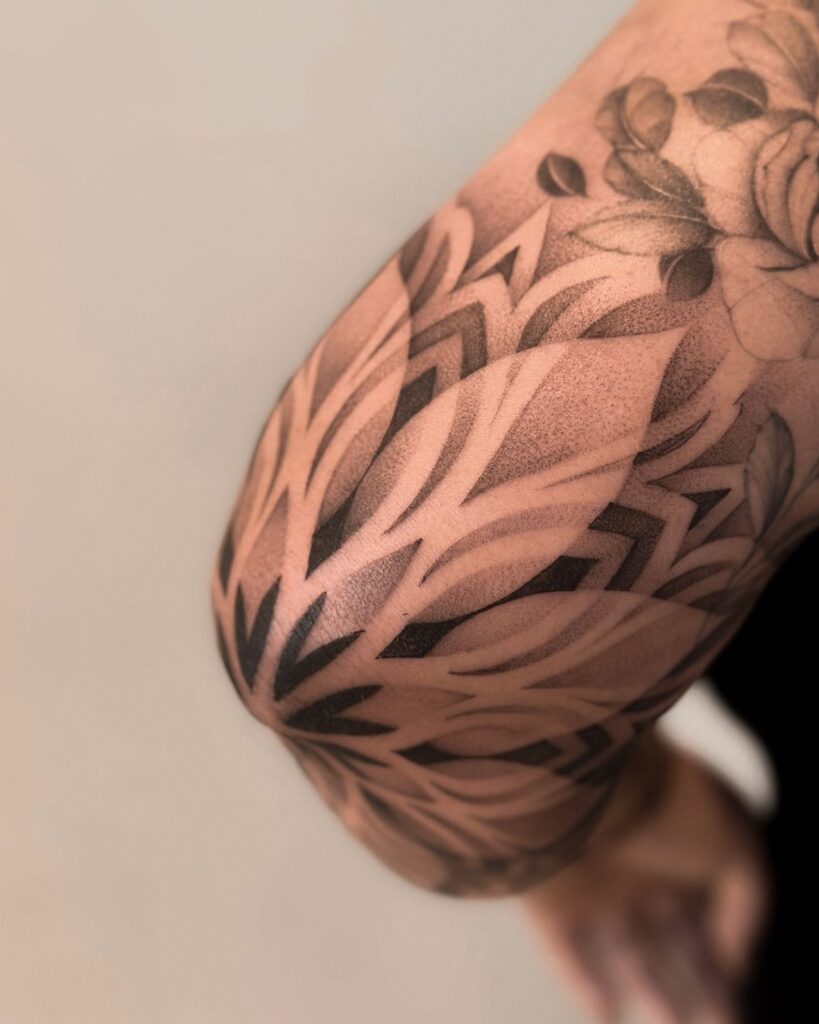 Abstract black and gray tattoo design on arm with floral and geometric patterns, close-up view.