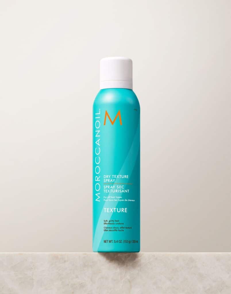 Aqua bottle of Moroccanoil Dry Texture Spray on a marble surface, ideal for adding volume and texture to hair.