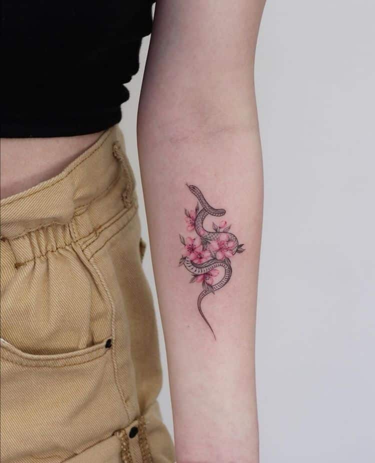 Snake and pink flower tattoo on a forearm, blending nature and art in minimalist design.