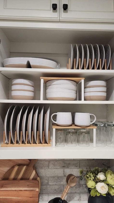 Organized kitchen cabinet with neatly stacked plates, bowls, mugs, and glasses on wooden holders; efficient storage for a tidy space.