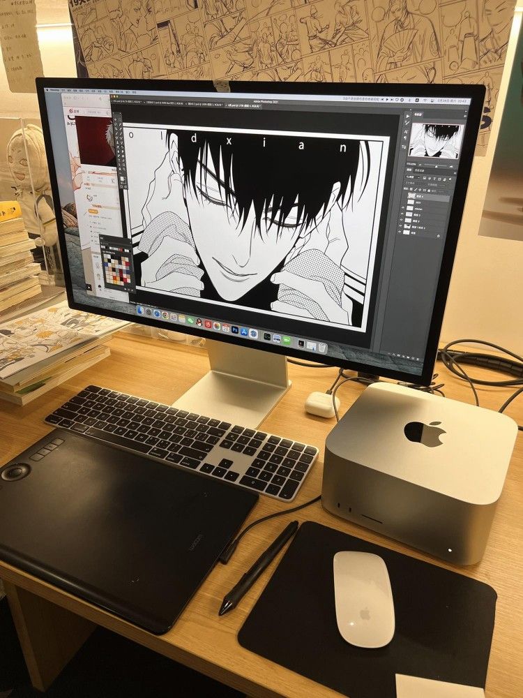 Graphic designer's workspace with computer displaying manga illustration, tablet, and drawing tools, surrounded by sketchboards and books.