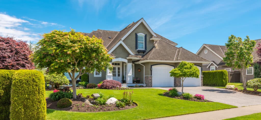 Beautiful suburban house with manicured lawn, colorful shrubs, and a clean driveway under a clear blue sky.