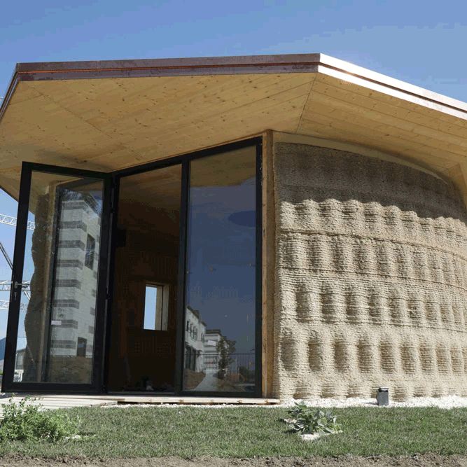 Modern eco-friendly house with textured walls and glass doors, showcasing sustainable architecture under a clear blue sky.
