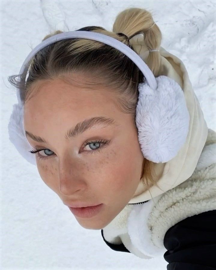 Person wearing cozy earmuffs and winter clothing in a snowy setting, looking upwards. Crisp winter fashion and snowy backdrop.