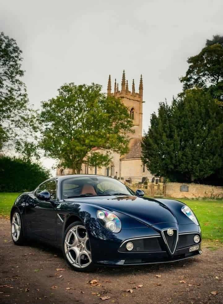 c5e4bd77280331d234698baedaacddc1 Sleek black sports car parked in front of a historic stone church, surrounded by lush trees under a cloudy sky. | Sky Rye Design Sleek black sports car parked in front of a historic stone church, surrounded by lush trees under a cloudy sky.