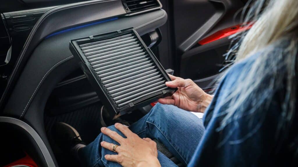 cabin_filter_install_xywovb Person inspecting a car cabin air filter inside a vehicle, highlighting automotive maintenance and air quality improvement. | Sky Rye Design Person inspecting a car cabin air filter inside a vehicle, highlighting automotive maintenance and air quality improvement.