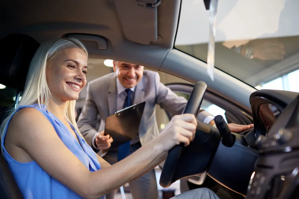 Woman test driving a car with salesman advising, showcasing automotive sales and customer experience in a dealership setting.