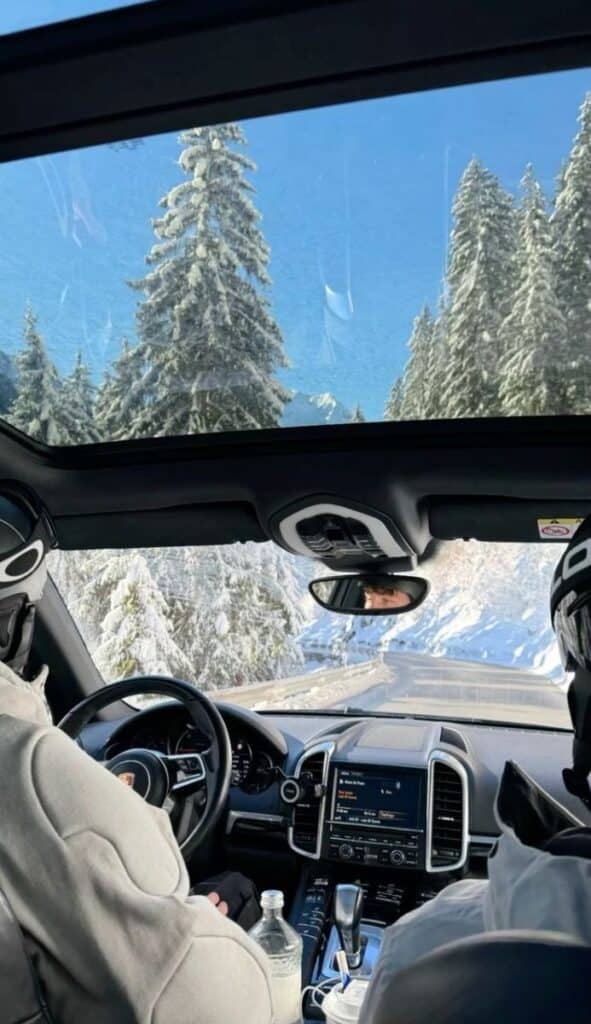 Driving through snowy mountains, two people enjoy a scenic winter road trip in a car with panoramic views and clear blue skies.