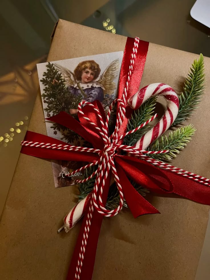 Christmas gift wrapped in brown paper with red ribbon, candy cane, evergreen sprigs, and an angel card for a festive holiday touch.