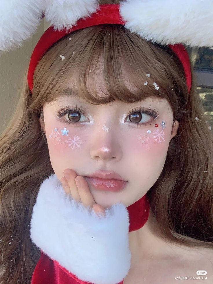 Young woman with festive makeup, featuring snowflake and star decorations, wearing red and white holiday attire with fluffy ears.