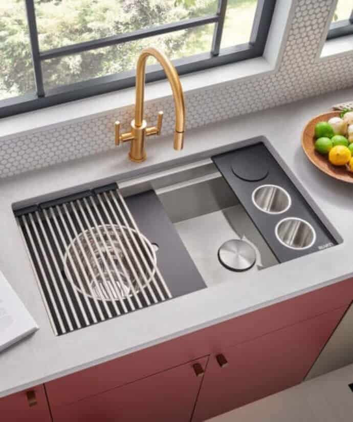 Modern kitchen sink with gold faucet, integrated cutting board, and red cabinets under a bright window. Stylish and functional design.