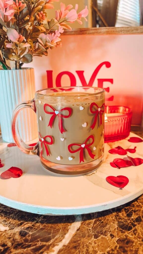 coquette valentines bows glass mug Festive Valentine's coffee mug with red bows, surrounded by heart decor, candle, and flowers on a marble table. Perfect for love-themed cafes. | Sky Rye Design Festive Valentine's coffee mug with red bows, surrounded by heart decor, candle, and flowers on a marble table. Perfect for love-themed cafes.