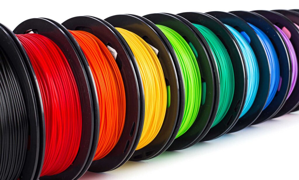 Colorful 3D printing filament spools in a row, featuring vibrant shades of black, red, orange, yellow, green, and blue.