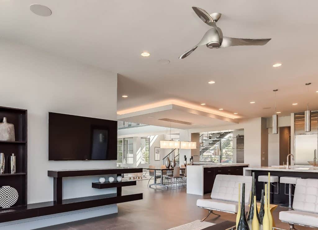 Modern living room and kitchen with sleek decor, recessed lighting, and a ceiling fan, showcasing open-plan contemporary interior design.
