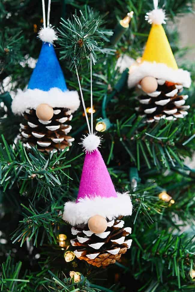 da6c2abbfc02b511c6e8fb4ed897f4bb Colorful pinecone gnome ornaments with felt hats hang on a Christmas tree, surrounded by twinkling lights, creating festive decor. | Sky Rye Design Colorful pinecone gnome ornaments with felt hats hang on a Christmas tree, surrounded by twinkling lights, creating festive decor.