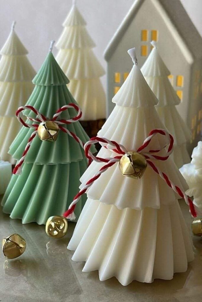 Festive Christmas tree-shaped candles with bows and bells, against a cozy background of small illuminated houses.