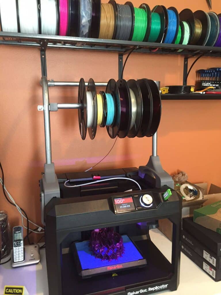 defb0199e6e3253f554da3575b0b2302 3D printer with colorful filament spools on shelves, printing an object. | Sky Rye Design 3D printer with colorful filament spools on shelves, printing an object.