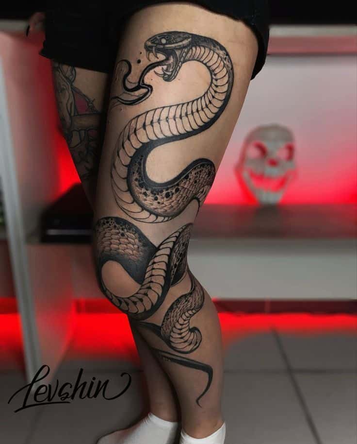 Intricate black cobra tattoo on thigh, showcasing detailed scales and fangs, with a glowing red background.
