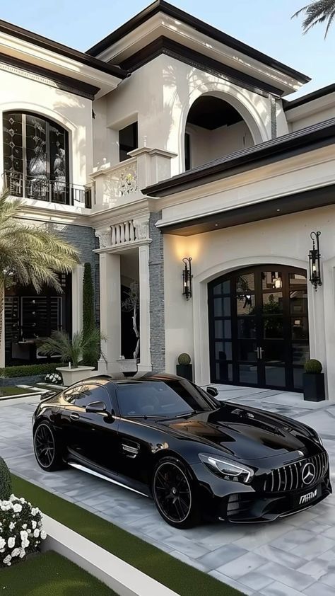 Luxury black sports car parked in front of an elegant mansion with large windows and manicured greenery, exuding sophistication.