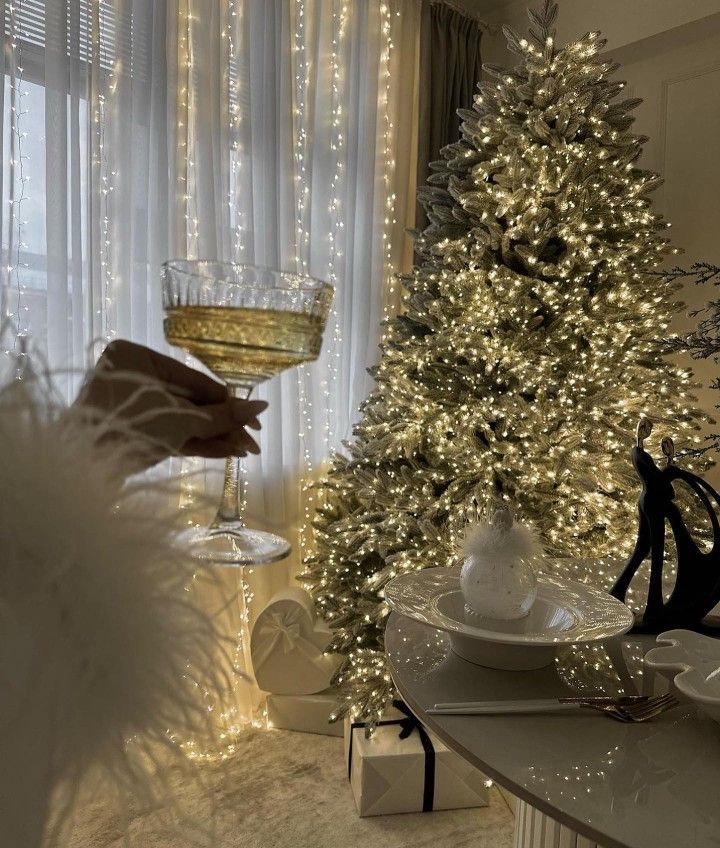 Elegant Christmas setting with a sparkling tree, champagne glass, and festive decor under fairy lights.