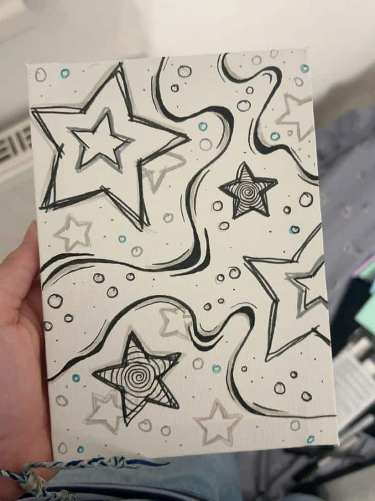 Hand holding a sketch of stars and swirls on canvas with black lines and blue accents, featuring a creative abstract starry design.
