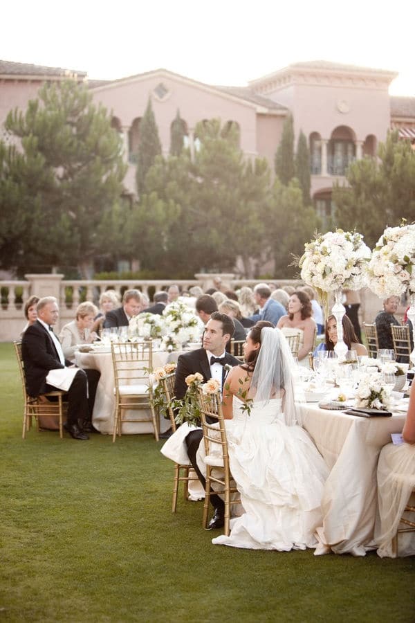 everything_ Elegant outdoor wedding reception with guests seated at tables, surrounded by lush greenery and floral arrangements, near a grand villa. | Sky Rye Design Elegant outdoor wedding reception with guests seated at tables, surrounded by lush greenery and floral arrangements, near a grand villa.