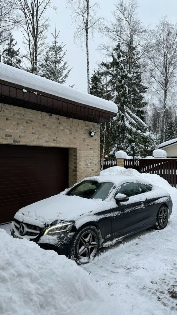 f2756a9e5106caa6a7761dba875ca01b A snow-covered car parked in front of a garage in a snowy winter landscape, surrounded by trees and a brick building. | Sky Rye Design A snow-covered car parked in front of a garage in a snowy winter landscape, surrounded by trees and a brick building.