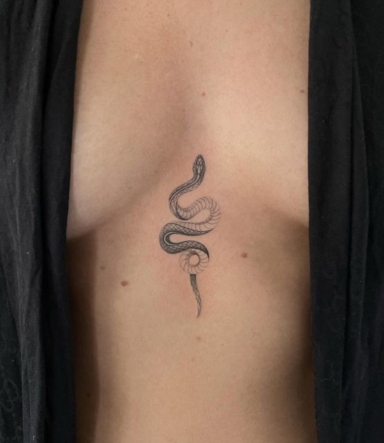 Minimalistic snake tattoo on bare chest, surrounded by dark fabric. Elegant design with fine lines.