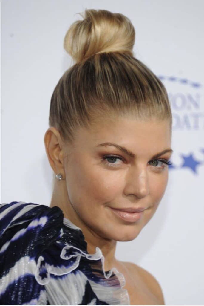 Elegant woman with updo, wearing a stylish dress at an event, smiling confidently against a light background.