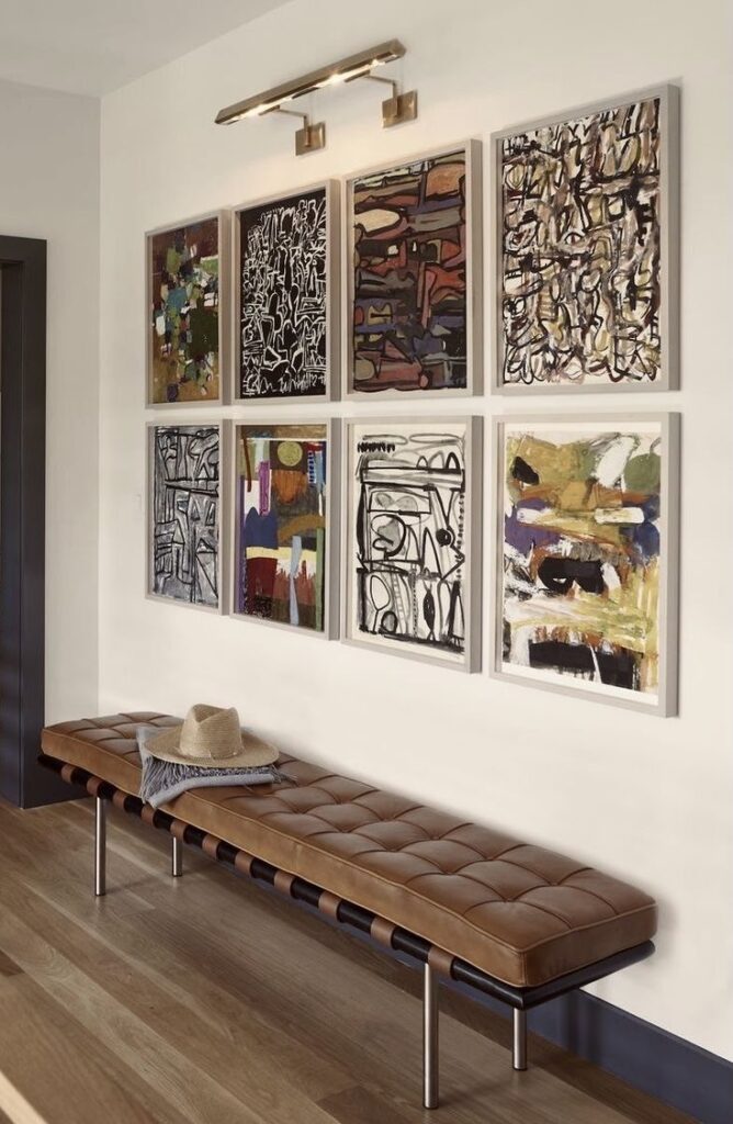 _ gallery Art gallery wall with abstract paintings above a brown leather bench in a modern interior hallway. | Sky Rye Design Art gallery wall with abstract paintings above a brown leather bench in a modern interior hallway.