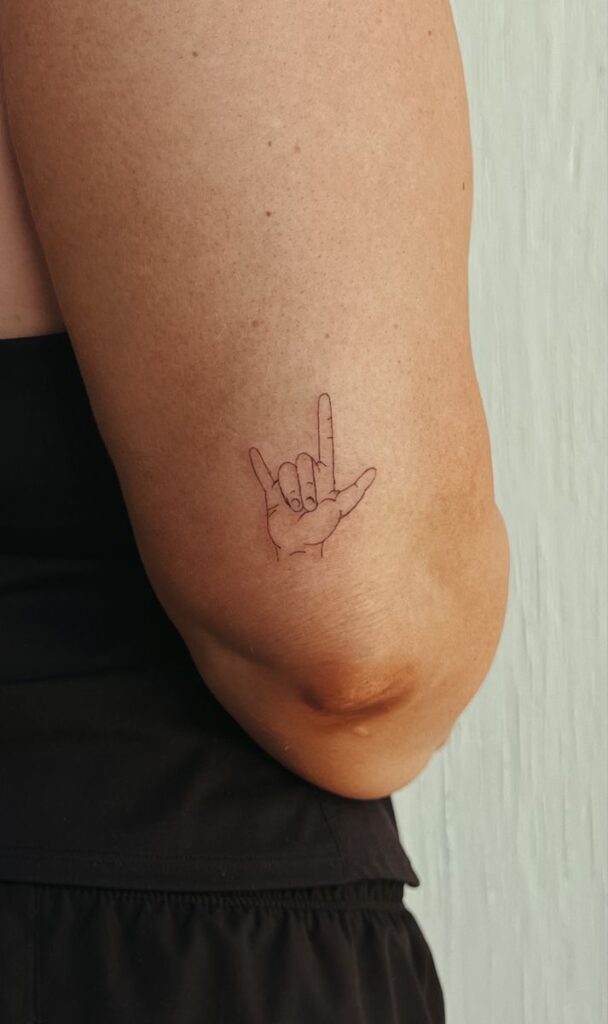 i love you tattoo -sign language Minimalist tattoo of a hand showing the I love you sign in sign language on upper arm, close-up view. | Sky Rye Design Minimalist tattoo of a hand showing the I love you sign in sign language on upper arm, close-up view.