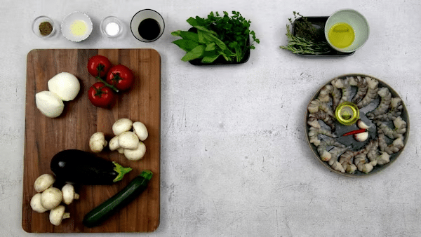 Fresh vegetables and herbs on a wooden board, with shrimp and oil on the side, ready for cooking a delicious and healthy meal.