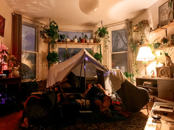 Cozy living room with indoor tent, surrounded by plants and soft lighting, creating a relaxing, whimsical atmosphere for relaxation.