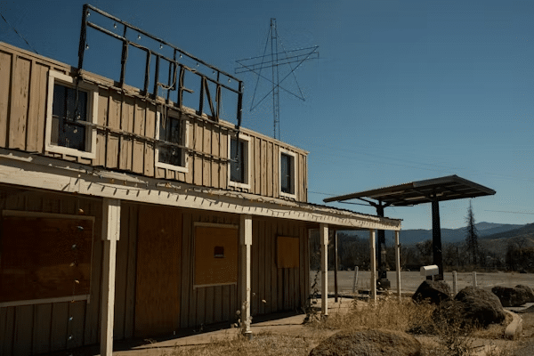 Abandoned wooden building with a OPEN sign on top, under a clear blue sky, suggesting desolation and rustic charm in a rural setting.