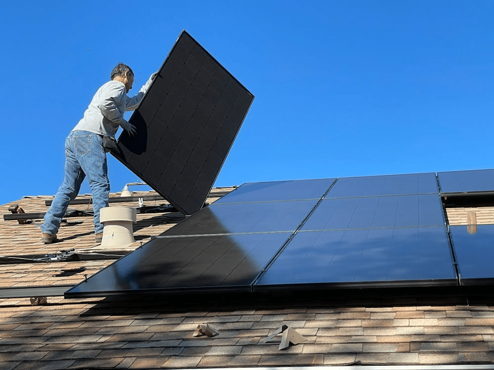 Installer placing solar panels on a rooftop under clear blue sky. Sustainable energy installation.