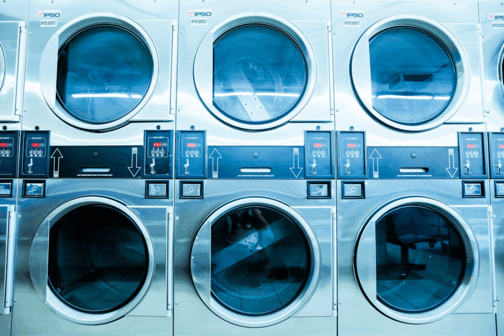 Six industrial washing machines in a bright laundromat, ready for use.