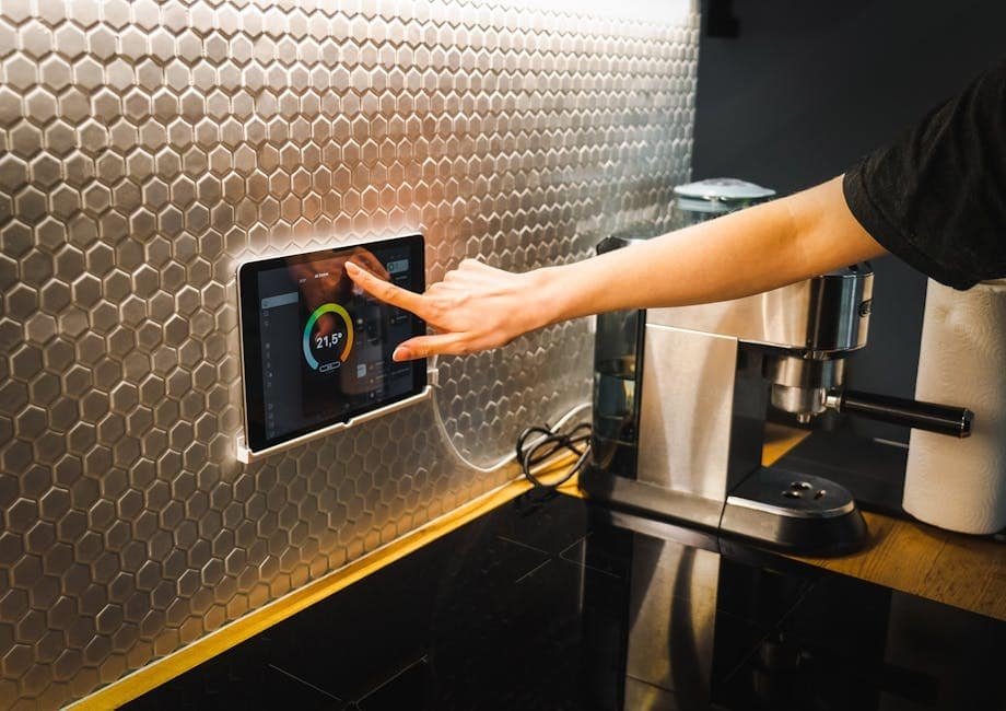 image Person adjusting smart home controls on a tablet embedded in a modern kitchen wall, next to a stainless steel espresso machine. | Sky Rye Design Person adjusting smart home controls on a tablet embedded in a modern kitchen wall, next to a stainless steel espresso machine.