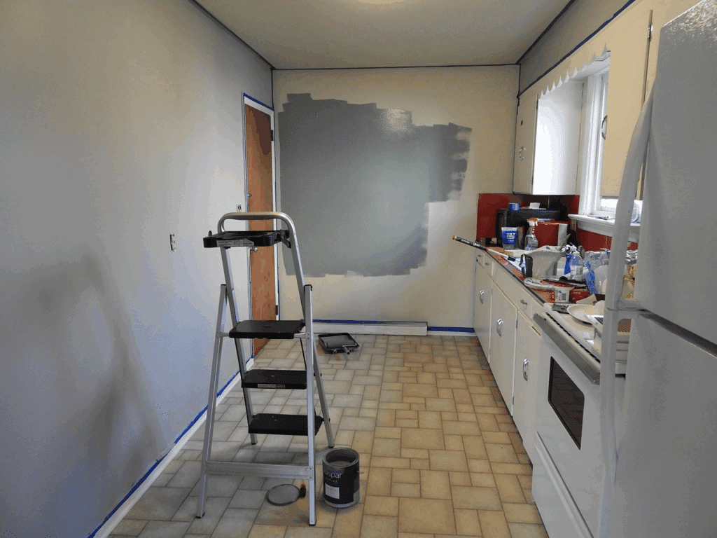 image Kitchen renovation in progress with fresh grey wall paint, ladder, and tools scattered on the counter and floor. | Sky Rye Design Kitchen renovation in progress with fresh grey wall paint, ladder, and tools scattered on the counter and floor.